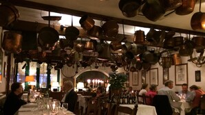 En restaurant med flere borde dækket til spisning, forskellige hængende krukker og en varm atmosfære indendørs.