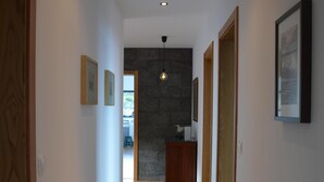 A hallway with wooden flooring, framed pictures on the walls, and a stone wall in the background. -  AtlanticWindow - Modern House, Stunning View (São Roque do Pico)