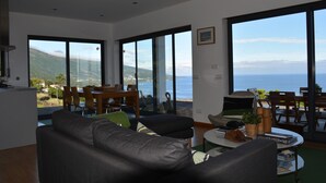 A modern living room with a large window offering a view of the sea and mountains. -  AtlanticWindow - Modern House, Stunning View (São Roque do Pico)