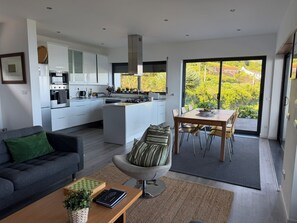 A modern kitchen with a central island, a dining area with a view, and a cozy seating area. -  AtlanticWindow - Modern House, Stunning View (São Roque do Pico)