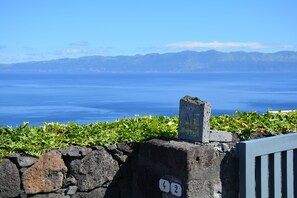 A stone wall with a sign indicating a path number, a view of a body of water, and distant mountains. -  AtlanticWindow - Modern House, Stunning View (São Roque do Pico)