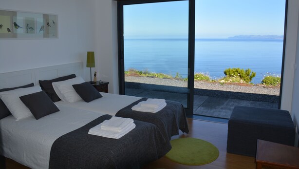 A modern bedroom with two beds, a view of the sea, and a green rug. -  AtlanticWindow - Modern House, Stunning View (São Roque do Pico)