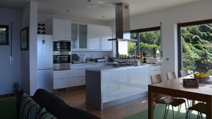 A modern kitchen with a central island, built-in appliances, and a view of greenery outside. -  AtlanticWindow - Modern House, Stunning View (São Roque do Pico)