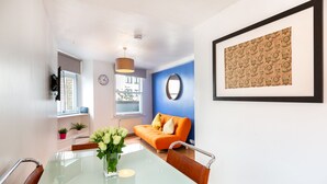 A modern living room with a glass dining table, orange sofa, and a framed artwork on the wall. - PRIVATE APARTMENT - HEART OF SHOREDITCH (London)