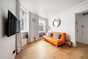 A modern living room with a flat-screen TV, a sofa with cushions, a round mirror, and a wooden floor. - PRIVATE APARTMENT - HEART OF SHOREDITCH (London)
