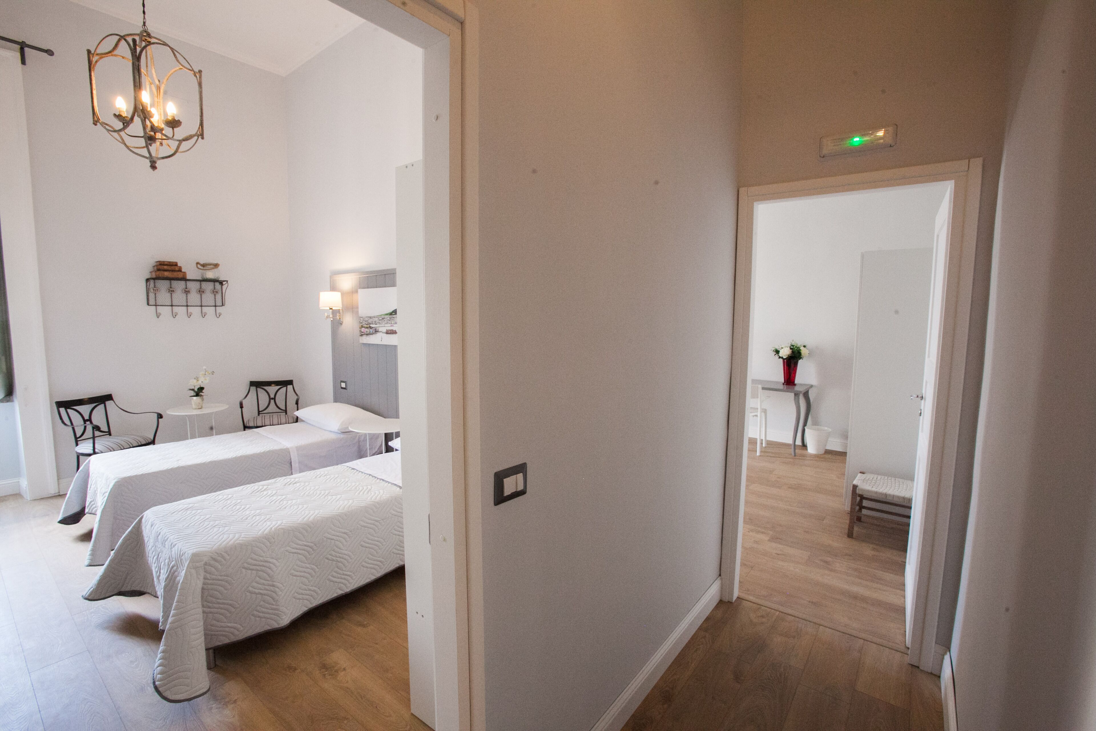 A hotel room with two beds, a chandelier, a small table with a vase, and a mirror on the wall.