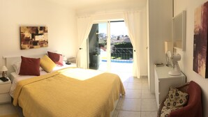 Une chambre à coucher avec un lit, des tables de chevet, une fenêtre avec des rideaux, un tableau au mur et une vue sur le balcon.
