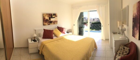 A bedroom with a bed, nightstands, a window with curtains, a painting on the wall, and a balcony view.