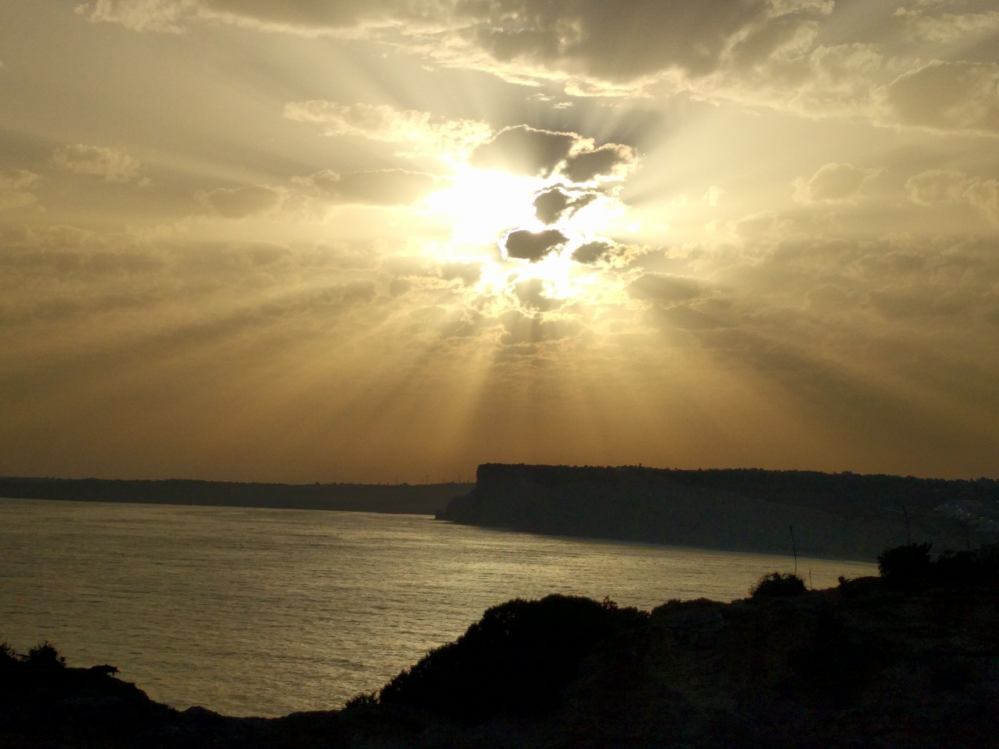 Un coucher de soleil sur un paysage côtier, avec une falaise à l'horizon.