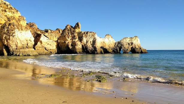 Une plage bordée de falaises rocheuses et aux vagues calmes.