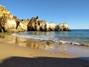 A beach with rocky cliffs and calm waves.
