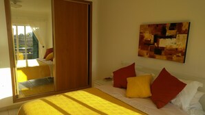 Une chambre avec un grand miroir, un lit avec une literie jaune et rouge, et un tableau accroché au mur.