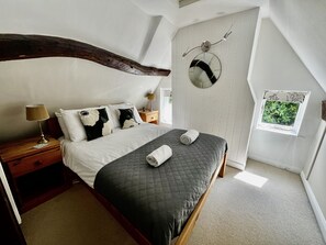 Un dormitorio con cama, mesita de noche, lámpara, espejo y ventana con vistas a follaje.