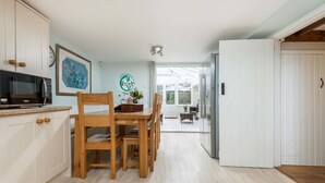 Ett modernt kök med vita skåp, ett matbord med stolar, en mikrovågsugn och en klocka på väggen.
