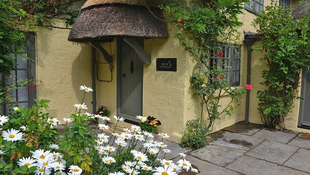 En stuga med ett halmtak, en dörr och en skylt med texten ”BECK COTTAGE”.