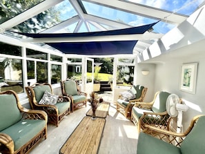 Uma sala de sol com móveis de vime, um ventilador e vista para o jardim.