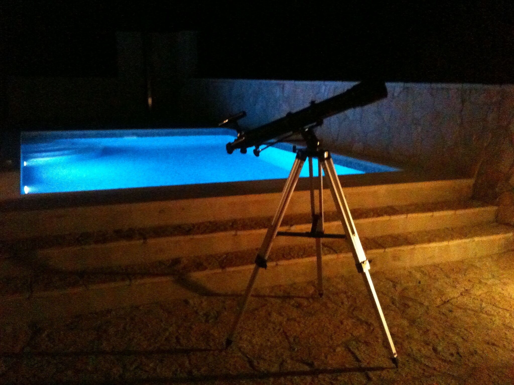 Ein Teleskop auf einem Stativ in der Nähe eines Schwimmbades bei Nacht.