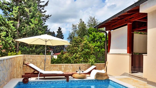 Une piscine entourée de murs de pierre et de verdure, avec des chaises longues et un parasol.