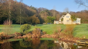 A house with a pond in front, surrounded by trees and a grassy area. - Spectacular setting in unspoilt East Devon, 15 minutes from Jurassic Coast. (Nr Honiton)