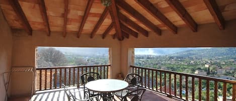 Een balkon met een houten plafond, een ronde tafel met stoelen en uitzicht op een landschap.