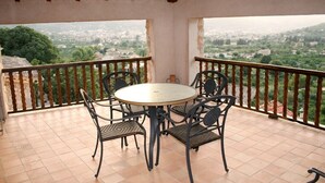 Ein Balkon mit rundem Tisch und Stühlen, der einen Blick auf eine Stadt und Hügel bietet.
