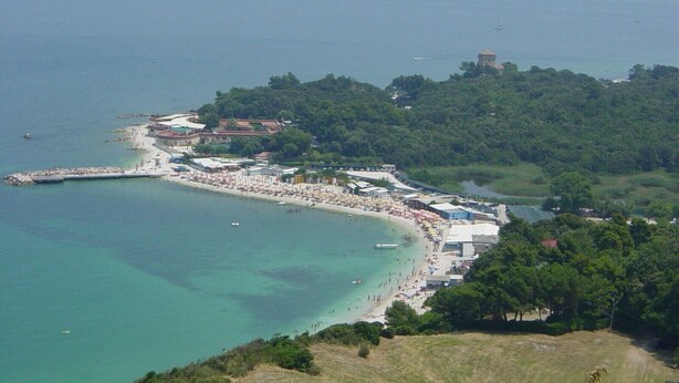 A coastal town with a beach, buildings, and a hill with a tower.