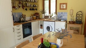 A kitchen with white cabinets, a wooden table, a wine bottle, and a bowl of fruit.