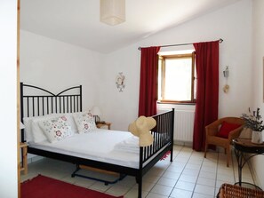 A bedroom with a bed, a window with curtains, a chair, and a small table with a plant.