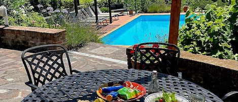 Un área de comedor al aire libre con una piscina de fondo.