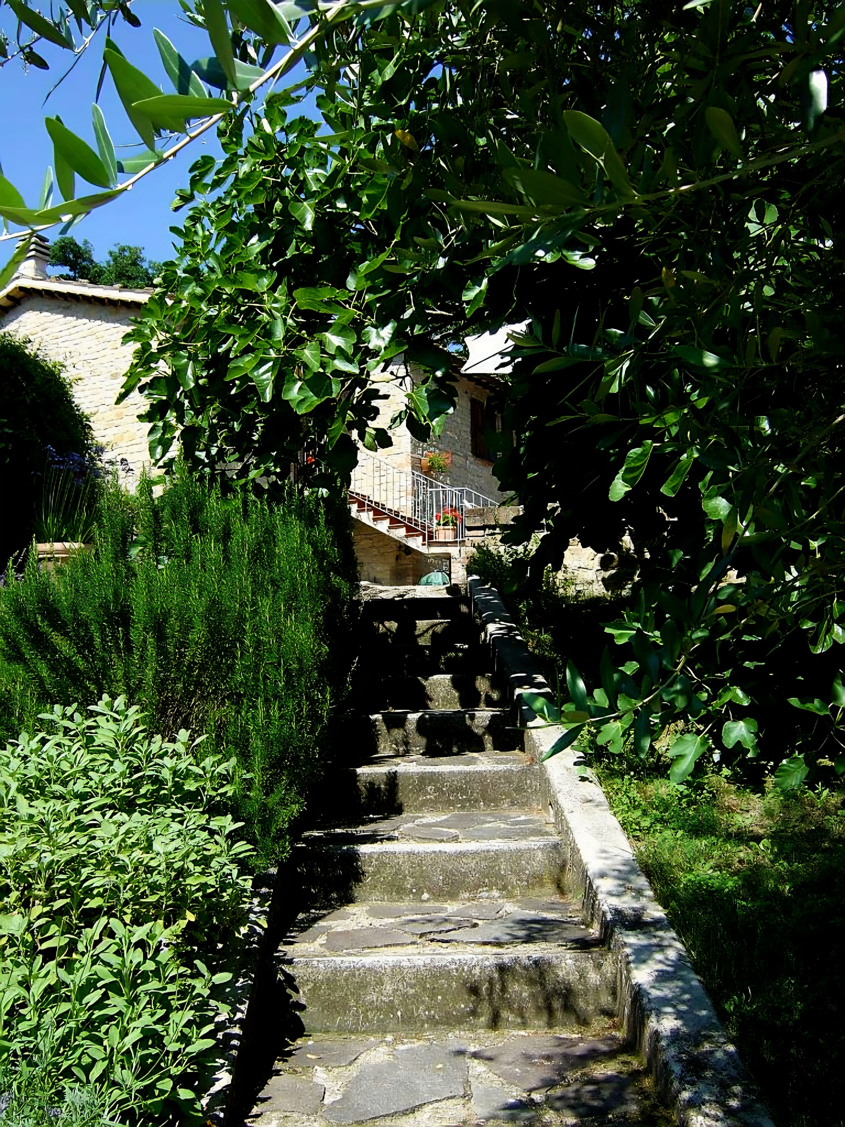 A stone staircase leading up to a building with a stone wall and a metal railing.