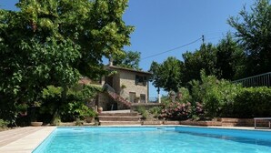 A swimming pool with clear water, surrounded by greenery and a stone building with a staircase.