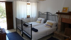 Une chambre avec deux lits, une fenêtre avec des rideaux, une cheminée et une vue sur la verdure.