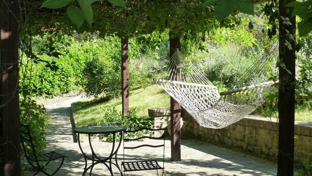 Uma rede sob uma pérgola, uma mesa de metal e cadeiras em um jardim.