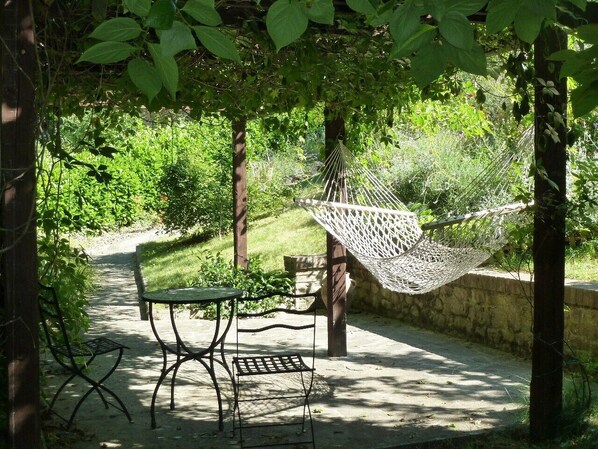 Un hamac sous une pergola, une table en métal et des chaises, le tout dans un cadre de jardin.