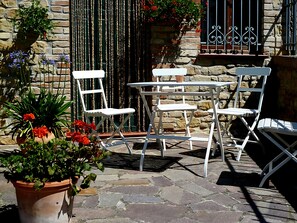 Un espace extérieur aménagé avec des chaises blanches et une table, entouré de plantes en pot et d’un mur de pierre.
