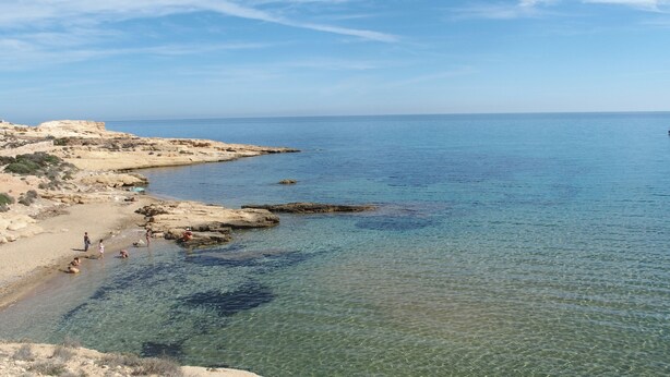 Una playa costera con aguas poco profundas y claras y terreno rocoso.