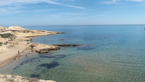 Una playa costera con aguas poco profundas y claras y terreno rocoso.