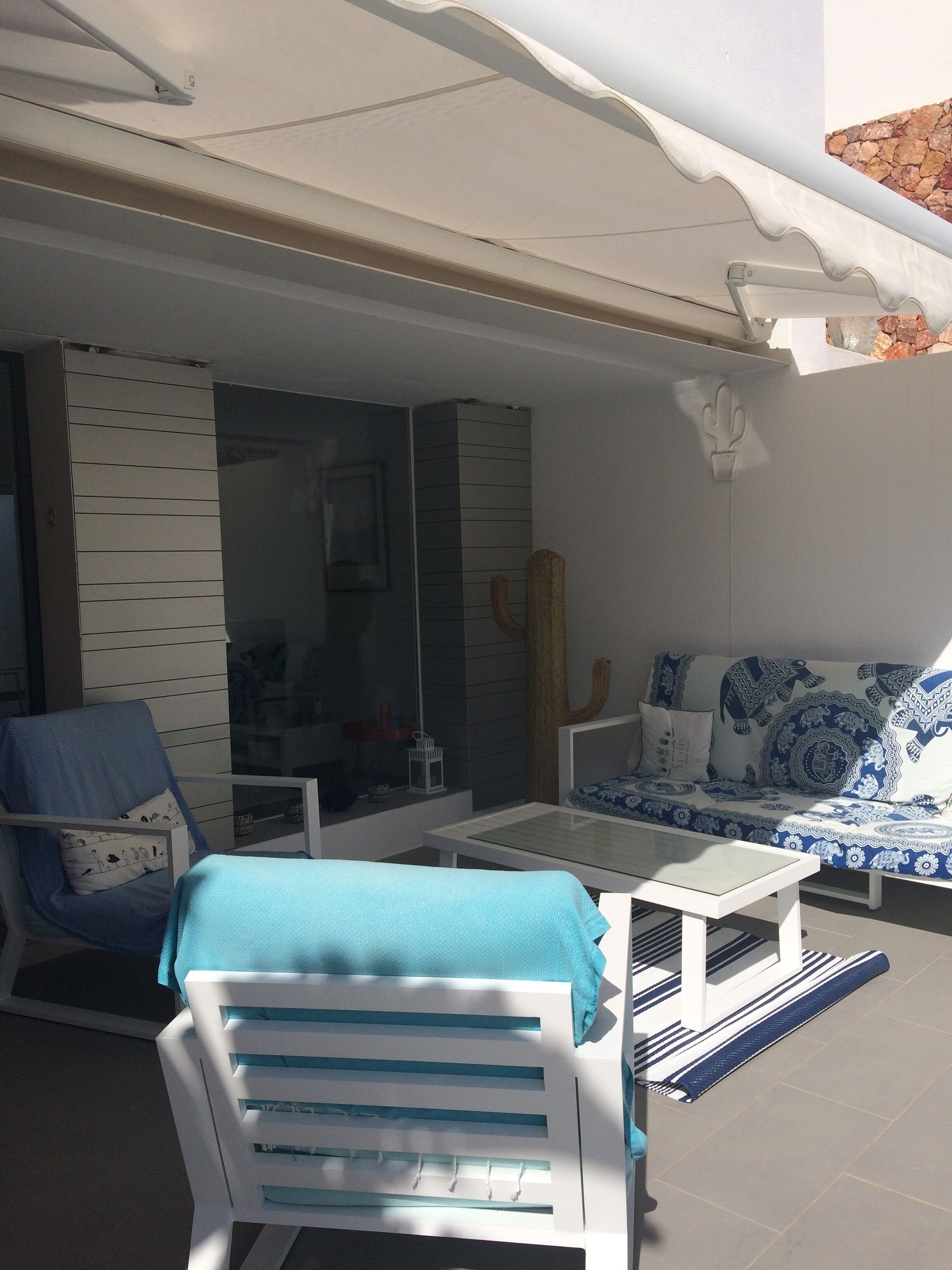 A sunlit patio with a white sofa, a blue chair, and a white table.