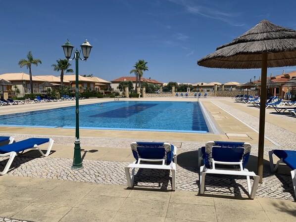 A swimming pool with lounge chairs and umbrellas, surrounded by buildings with tiled roofs.