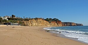A sandy beach with a rocky cliff and ocean waves.