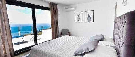 Un dormitori amb un llit gran, vista al mar i dos quadres al mur.