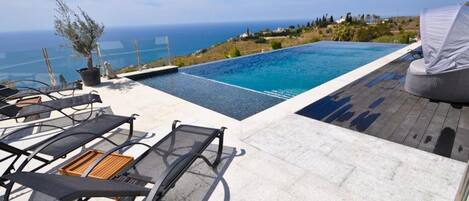 A rooftop infinity pool with lounge chairs and a view of the ocean.