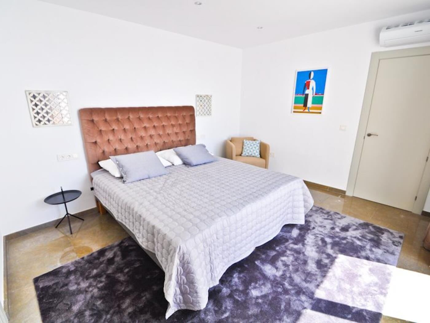 A bedroom with a large bed, a chair, a small table, and a door.
