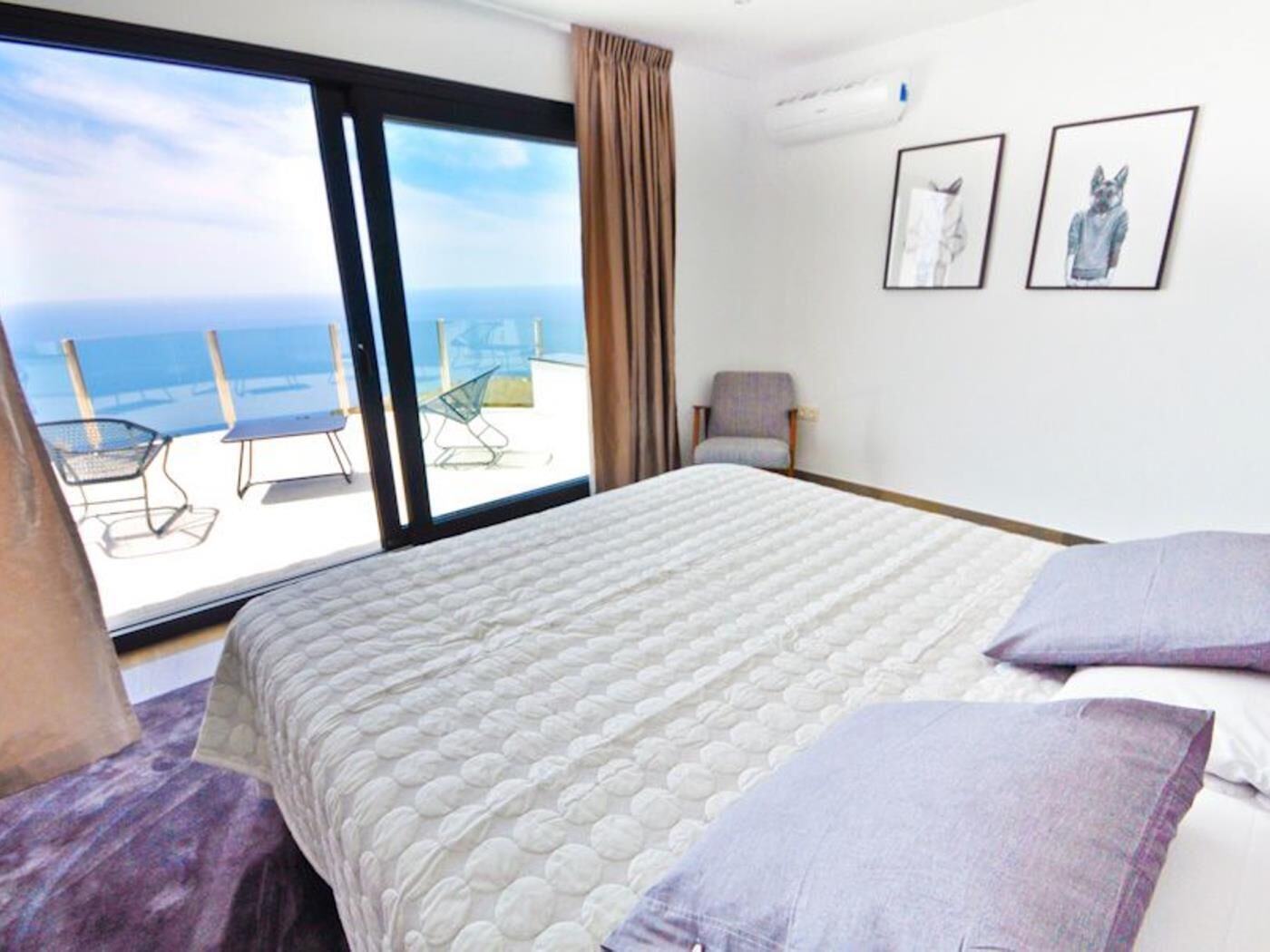 Une chambre d’hôtel avec un grand lit, une chaise et une vue sur l’océan, accessible par une porte-fenêtre coulissante.