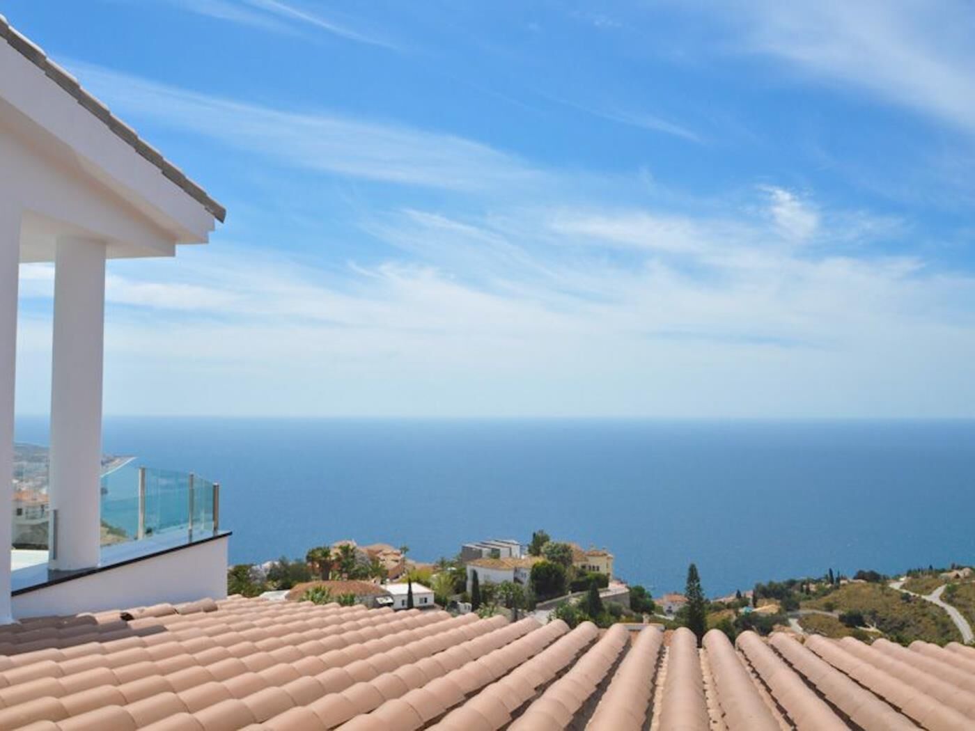 Vista costeira com telhados de terracota, céu claro e mar ao longe.