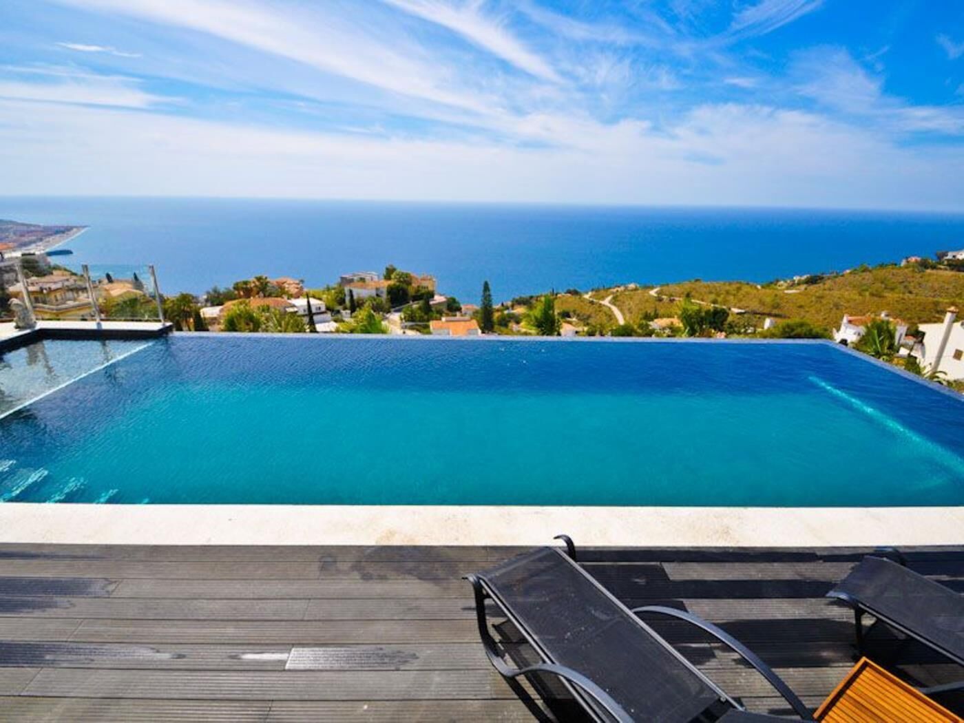 A rooftop infinity pool with a clear view of the sea and a deck with lounge chairs.