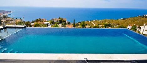 A rooftop infinity pool with a clear view of the sea and a deck with lounge chairs.