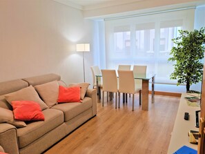 A modern living room with a beige sofa, red cushions, a glass dining table with chairs, a floor lamp, and a potted plant. - EXCLUSIVE APARTMENT SEASIDE BEACH ZURRIOLA (Donostia)