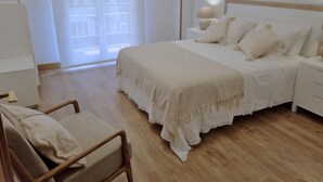 A bedroom with a bed, bedside tables, a chair, and a window with a view of buildings. - EXCLUSIVE APARTMENT SEASIDE BEACH ZURRIOLA (Donostia)