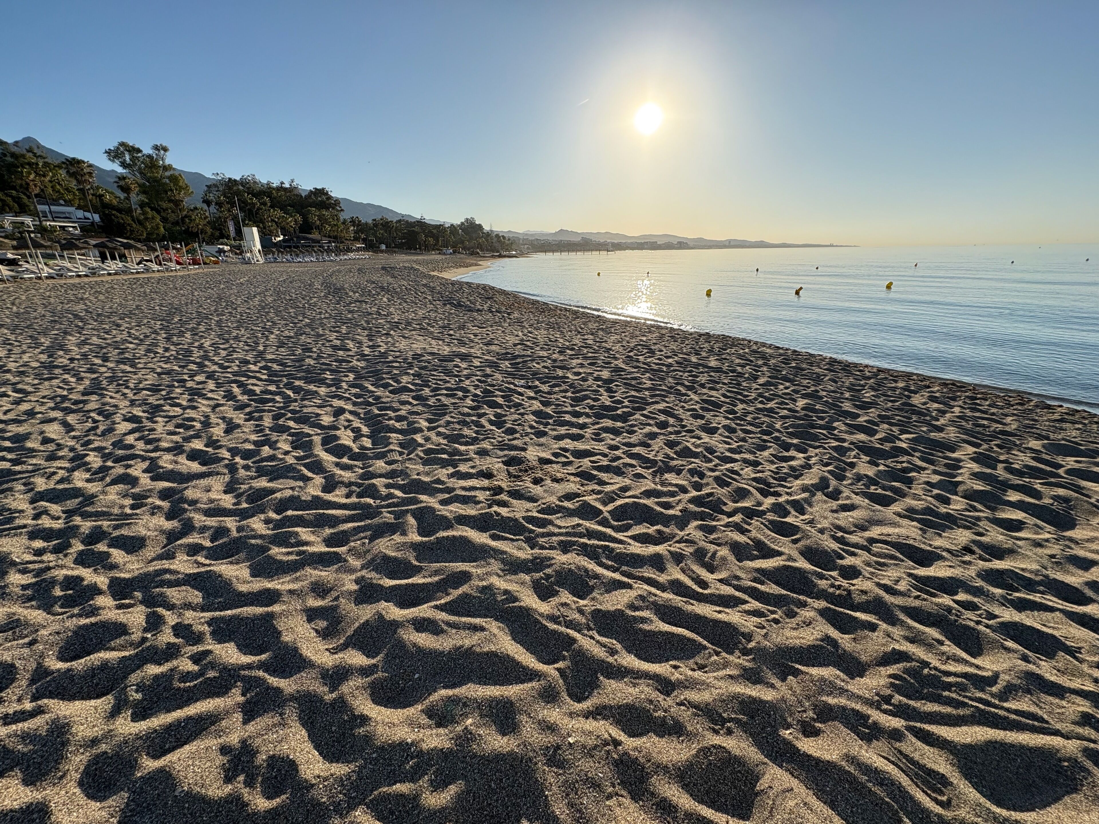 A beach with a clear sky and the sun shining.
